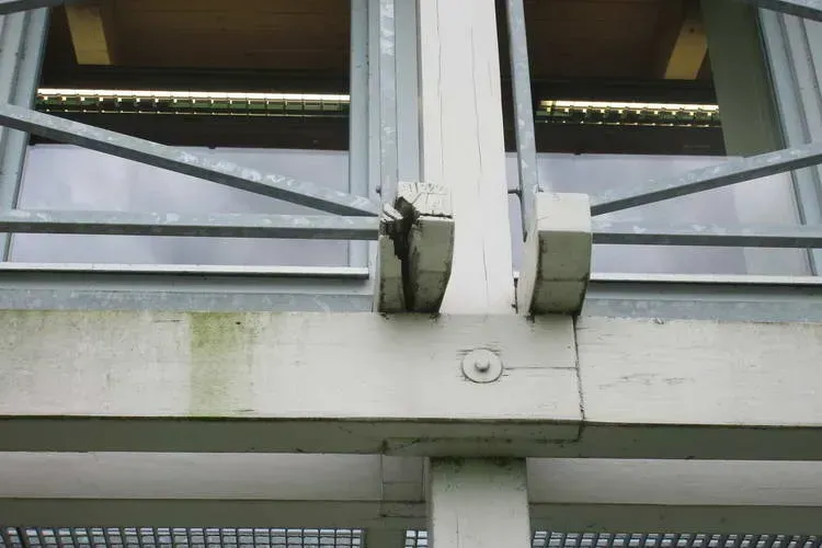 Zimmerei Andreas Karl GmbH - Stahlstreben auf einem weiß gestrichenen Holzbalken vor Fenstern