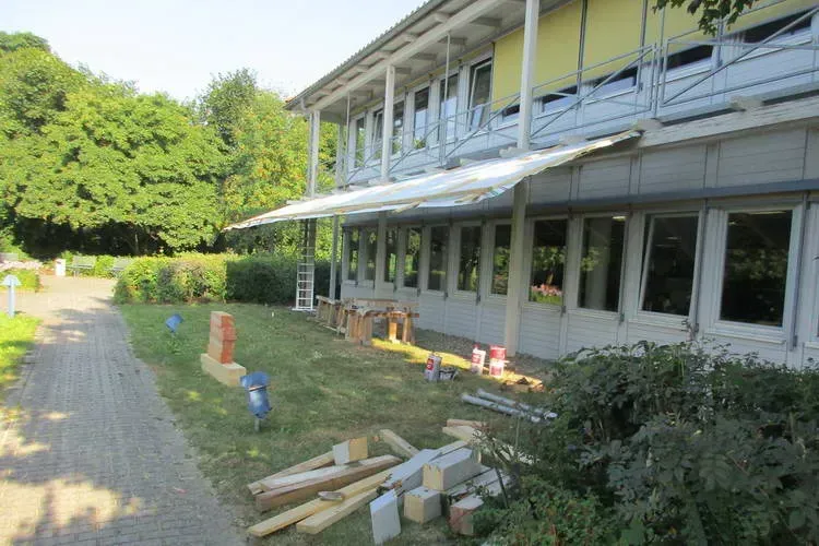 Zimmerei Andreas Karl GmbH - Altes Gebäude vor einer grünen Wiese mit Pfad, Baumaterial auf dem Boden