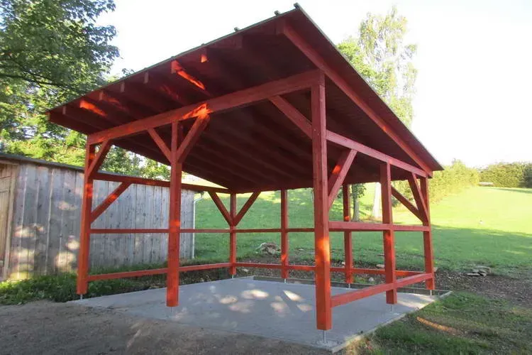 Zimmerei Andreas Karl GmbH - Carport aus rot gestrichenem Holz vor einer grünen Wiese