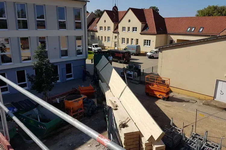 Zimmerei Andreas Karl GmbH - LKW zwischen mehreren Gebäuden liefert Holzbauteile an