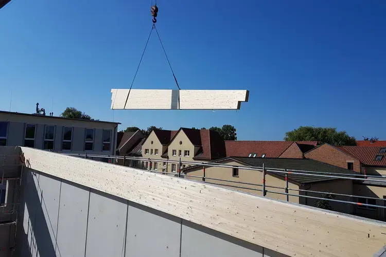 Zimmerei Andreas Karl GmbH - Holzbauteil hängt vor blauem Himmel am Seil eines Baukrans