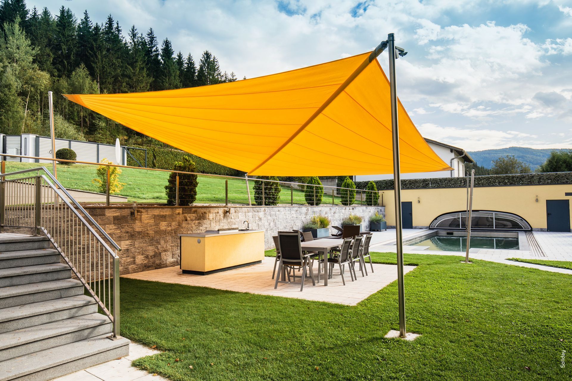 Un grande ombrellone giallo copre un patio con tavoli e sedie.