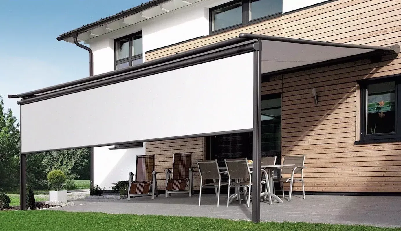 Una casa con un patio con tavoli e sedie sotto una tenda da sole bianca.