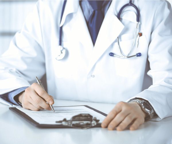 Un médico está escribiendo en un portapapeles con un bolígrafo.
