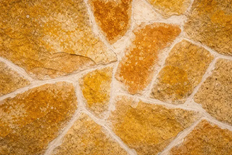 Primer plano de una pared de piedra con piedras irregulares en tonos dorados colocadas en lechada blanca.
