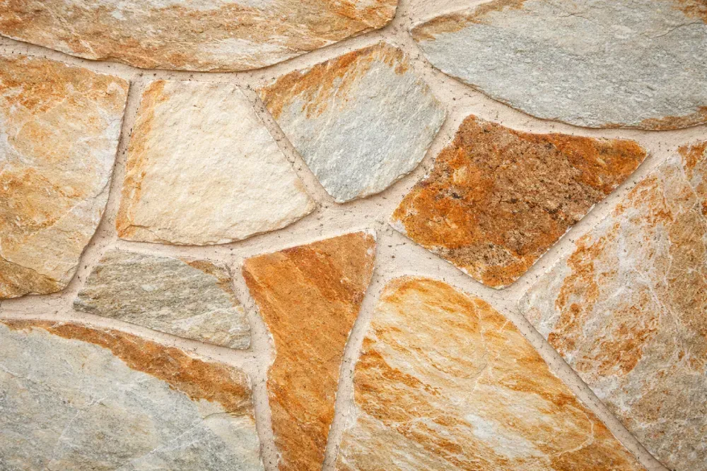 Azulejo de piedra con formas irregulares en tonos tostados, marrones y grises, separados por una lechada clara.