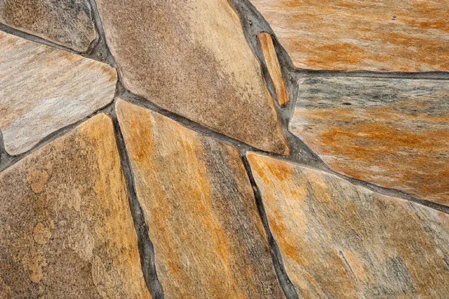 Primer plano de un piso de baldosas de piedra con baldosas de forma irregular, de color tostado y dorado y lechada gris.