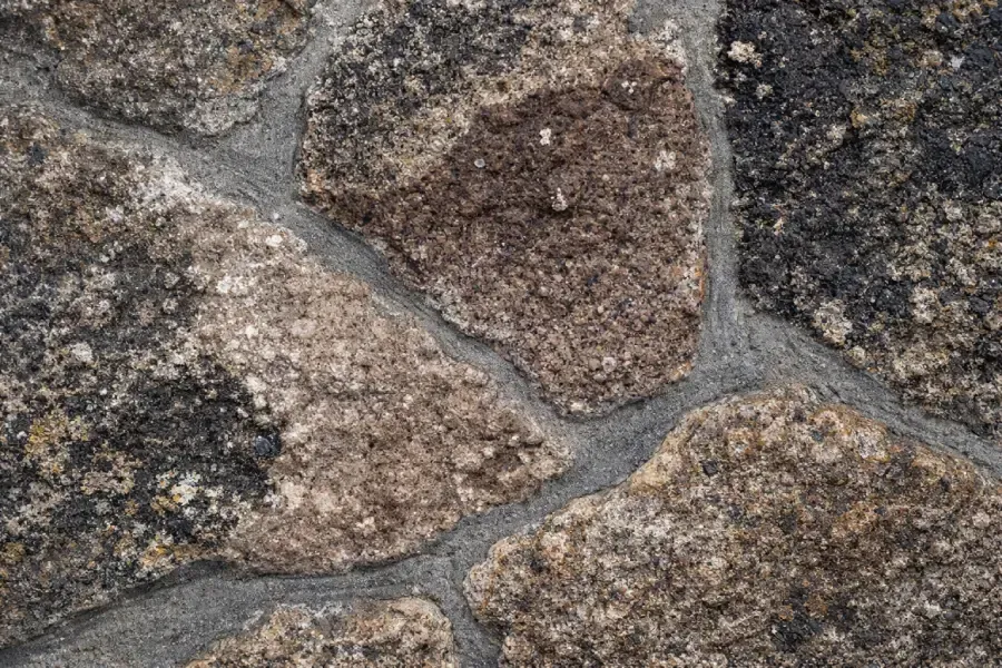 Primer plano de muro de piedra con piedras irregulares de color marrón y negro separadas por mortero gris.