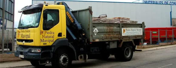 Camión amarillo con grúa estacionado en la calle frente a un edificio con texto en español.
