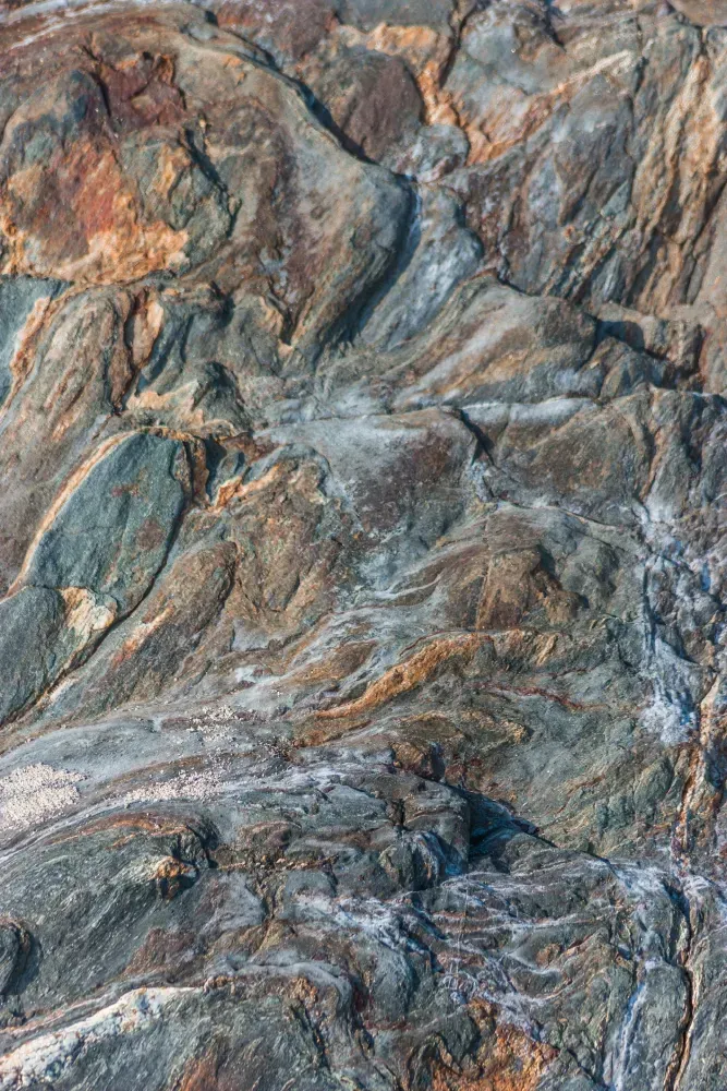 Pared de roca texturizada con capas de tonos grises, marrones y naranjas.