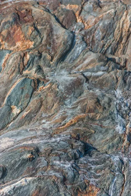 Pared de roca texturizada con capas de tonos grises, marrones y naranjas.