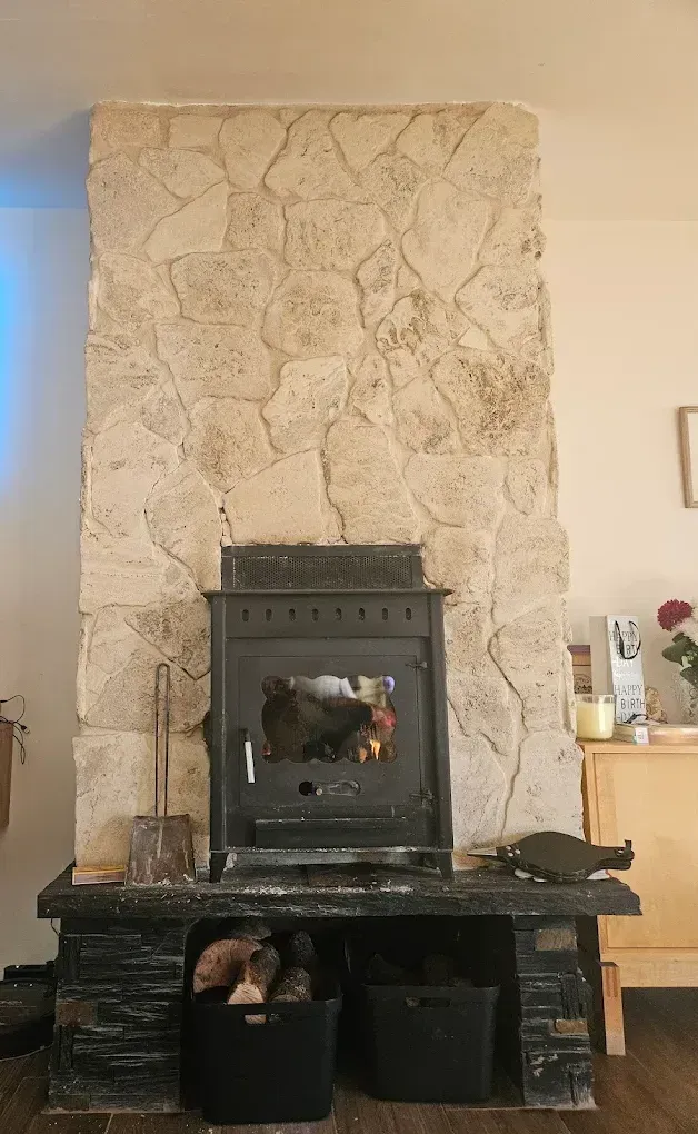 Chimenea con fuego ardiente, estufa negra, marco de piedra, leñero debajo.