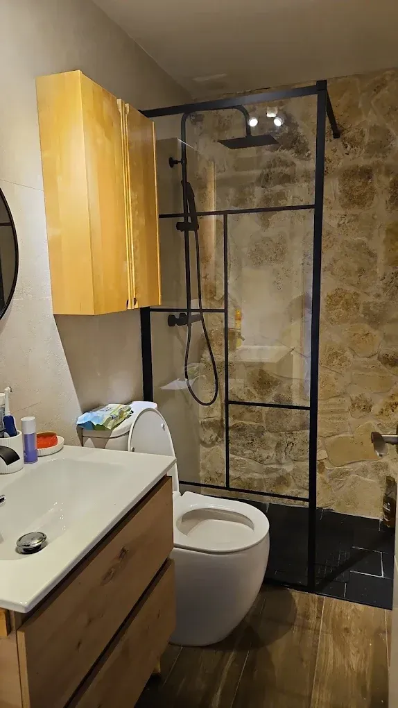 Baño con ducha de cristal, tocador de madera y un mueble de madera encima del inodoro.