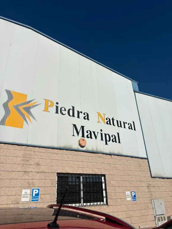 Edificio con las palabras “Piedra Natural Mavipal” en negro y amarillo, sobre una pared blanca y un cielo azul.