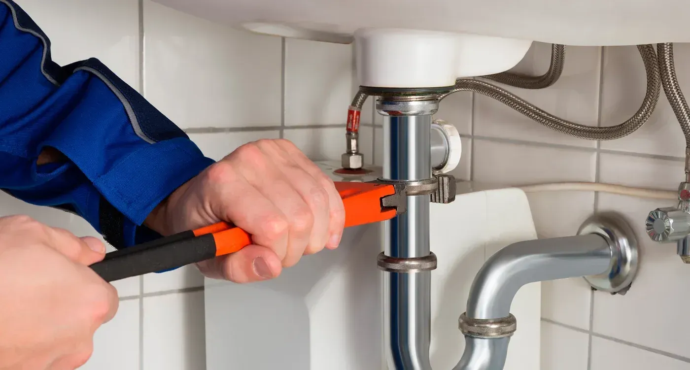 Fontanero usando una llave inglesa en las tuberías de un fregadero. Mono azul con mangas.