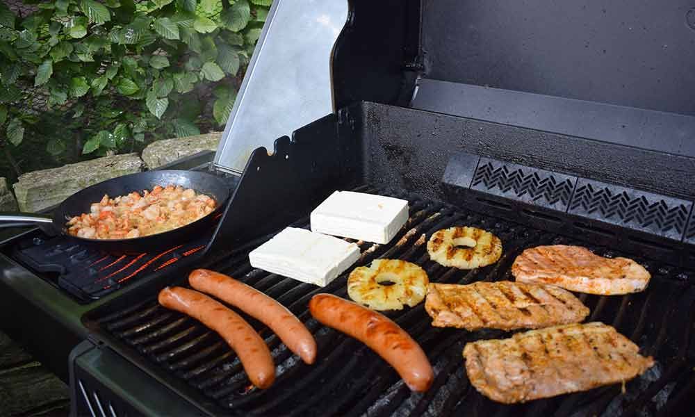 Ein Grill mit Fleisch, Wurst, Käse und Ananas darauf.