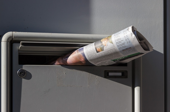Journal dans une boîte aux lettres grise, partiellement inséré.