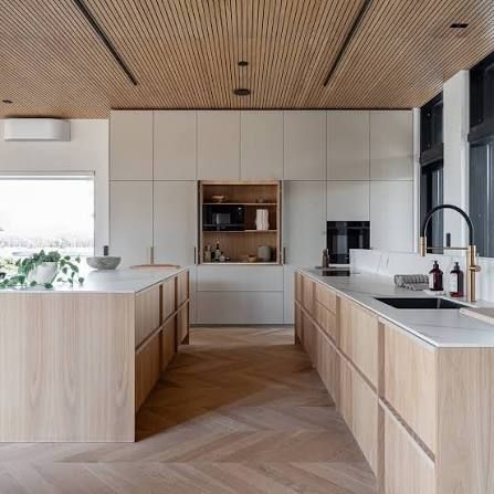 Esta moderna cocina cuenta con armarios de madera, una isla blanca, suelos en espiga y un techo de madera texturizada.