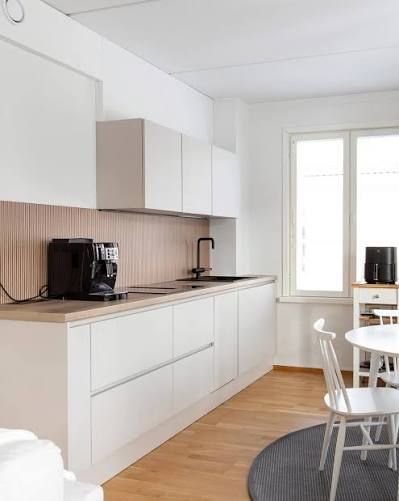 Cocina moderna con armarios blancos mate, salpicadero de madera, electrodomésticos negros y una mesa de comedor