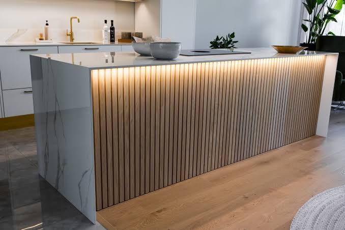 Una isla de cocina con un frontal de madera con listones, acentuado por una cálida iluminación LED
