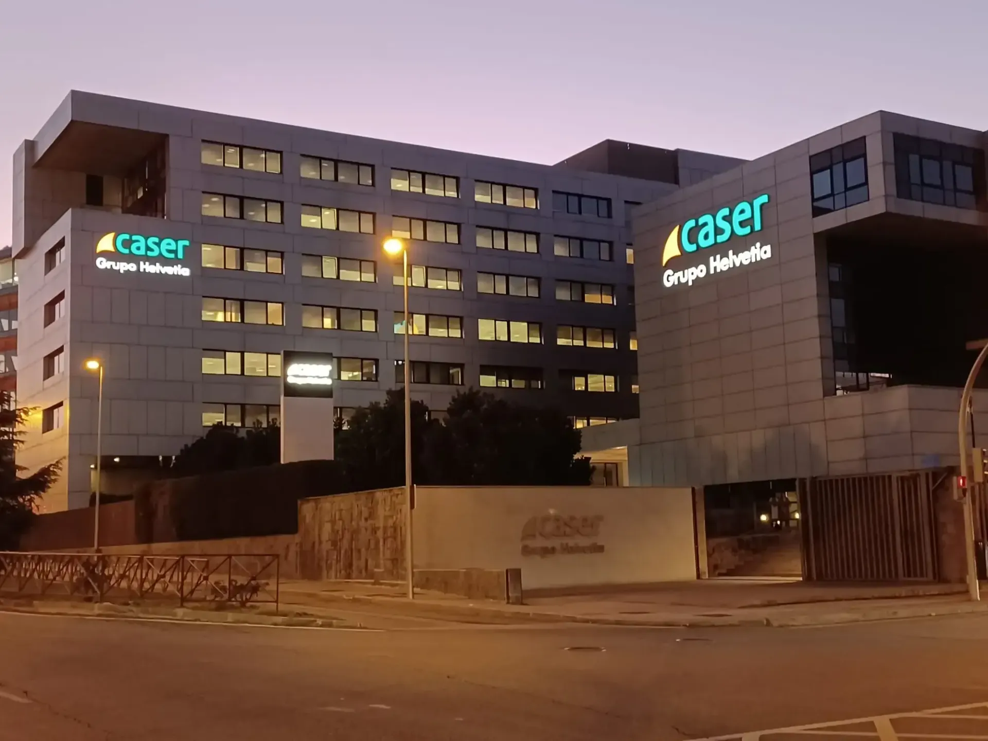 Exterior del edificio Caser Grupo Helvetia, iluminado al anochecer. Fachada gris y blanca, grandes letreros verdes de Caser.