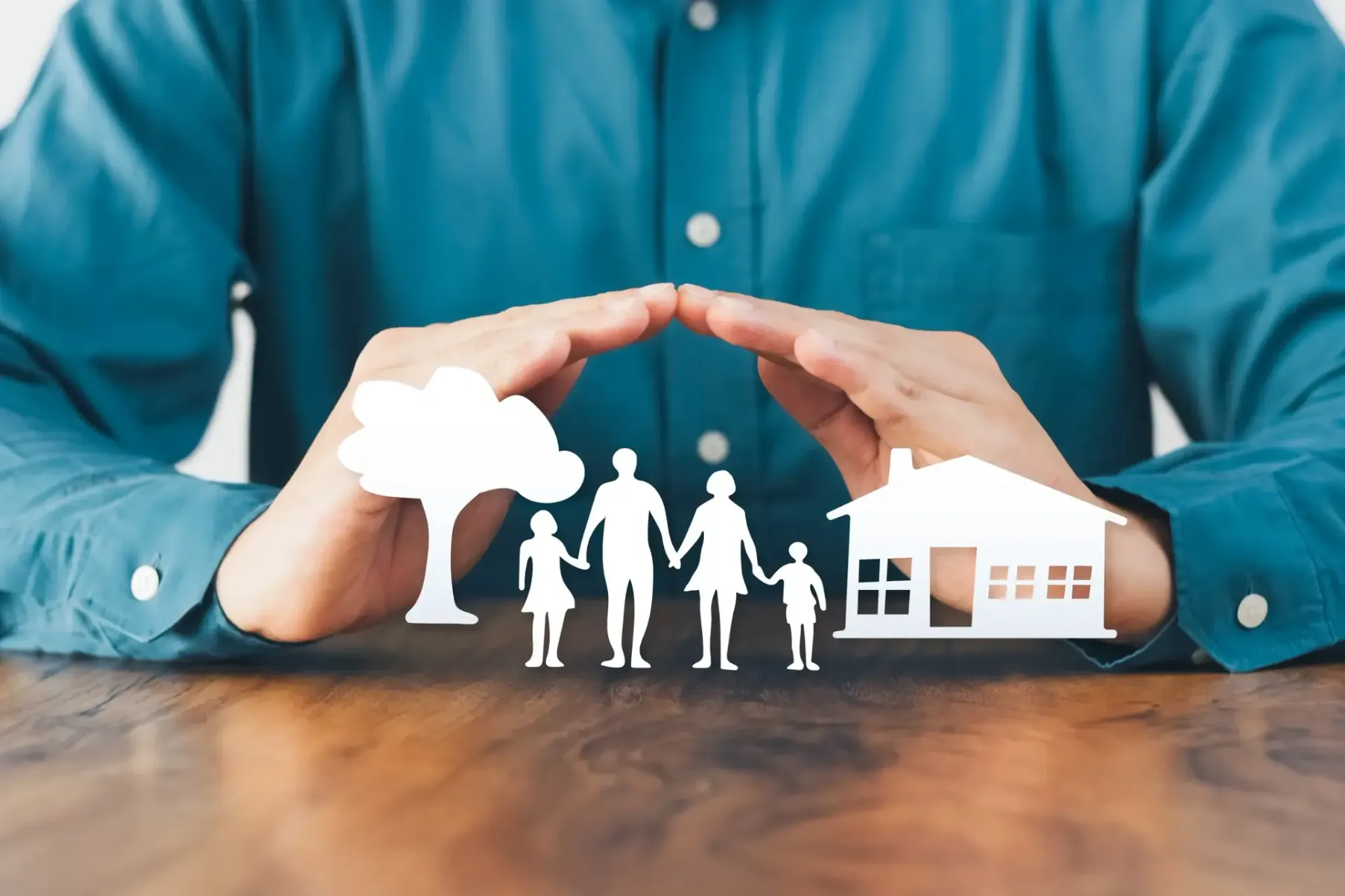 Manos protegiendo recortes de papel de una familia, una casa y un árbol.