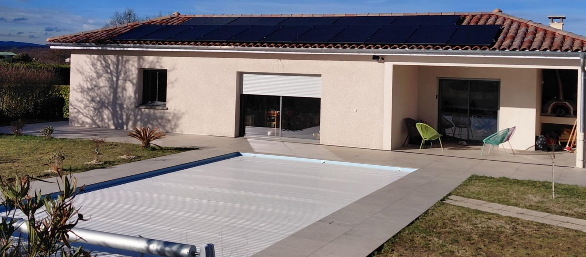 Des panneaux solaires sur un toit gris foncé se détachant sur un ciel bleu avec des nuages et des arbres.