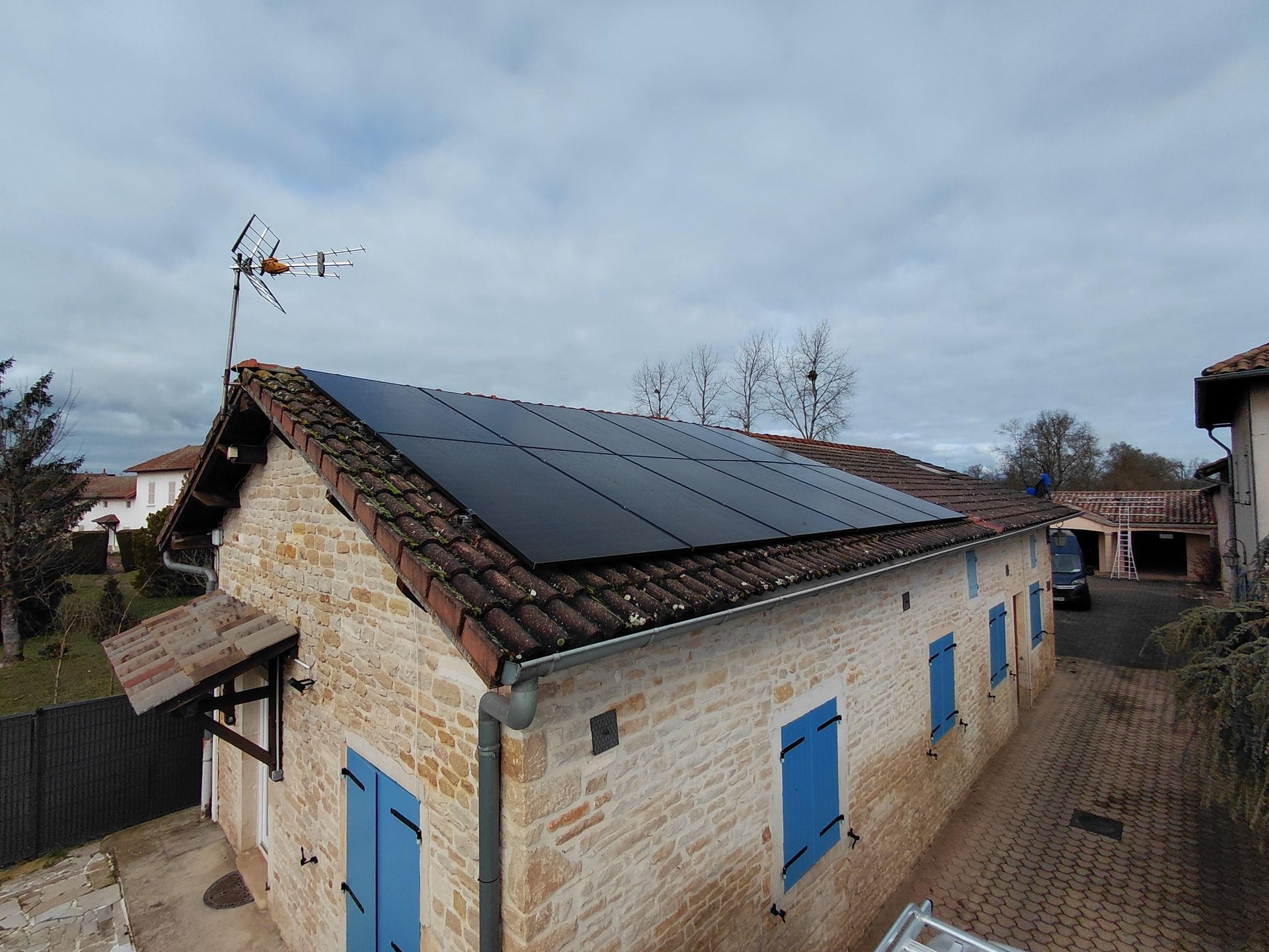 Maison avec panneaux solaires sur un toit de tuiles rouges sous un ciel bleu nuageux.