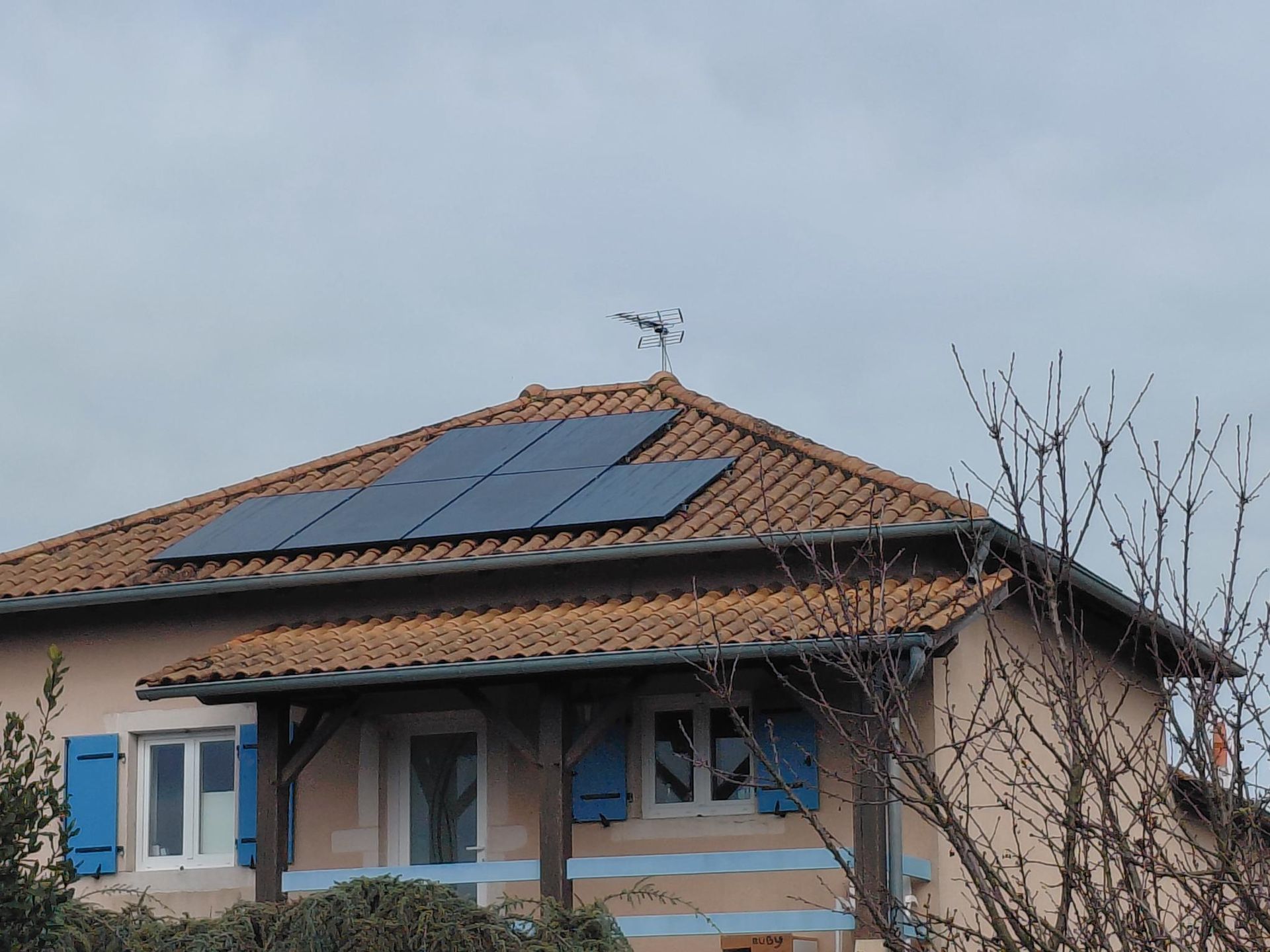 Des ouvriers installent des panneaux solaires sur le toit d'une maison, sous un ciel bleu nuageux.