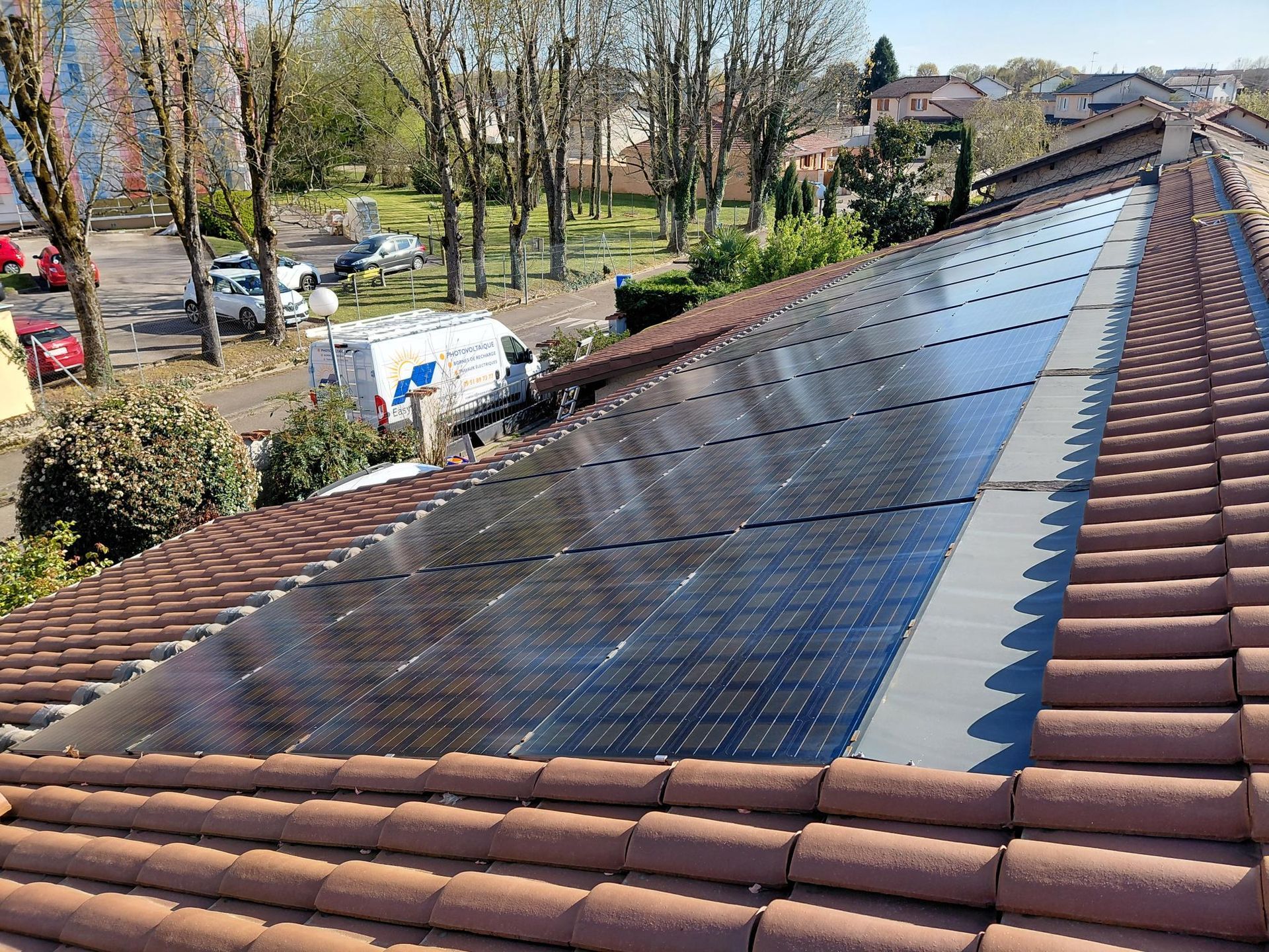 Des ouvriers installent des panneaux solaires sur le toit d'une maison sous un ciel bleu.