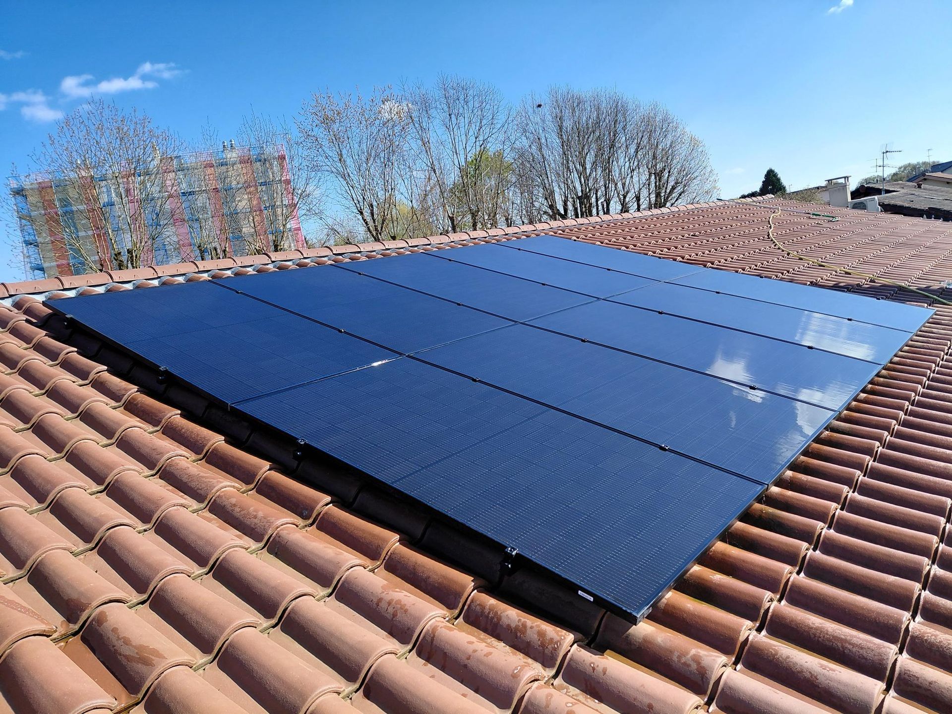 Des ouvriers installent des panneaux solaires sur le toit d'une maison sous un ciel bleu nuageux.