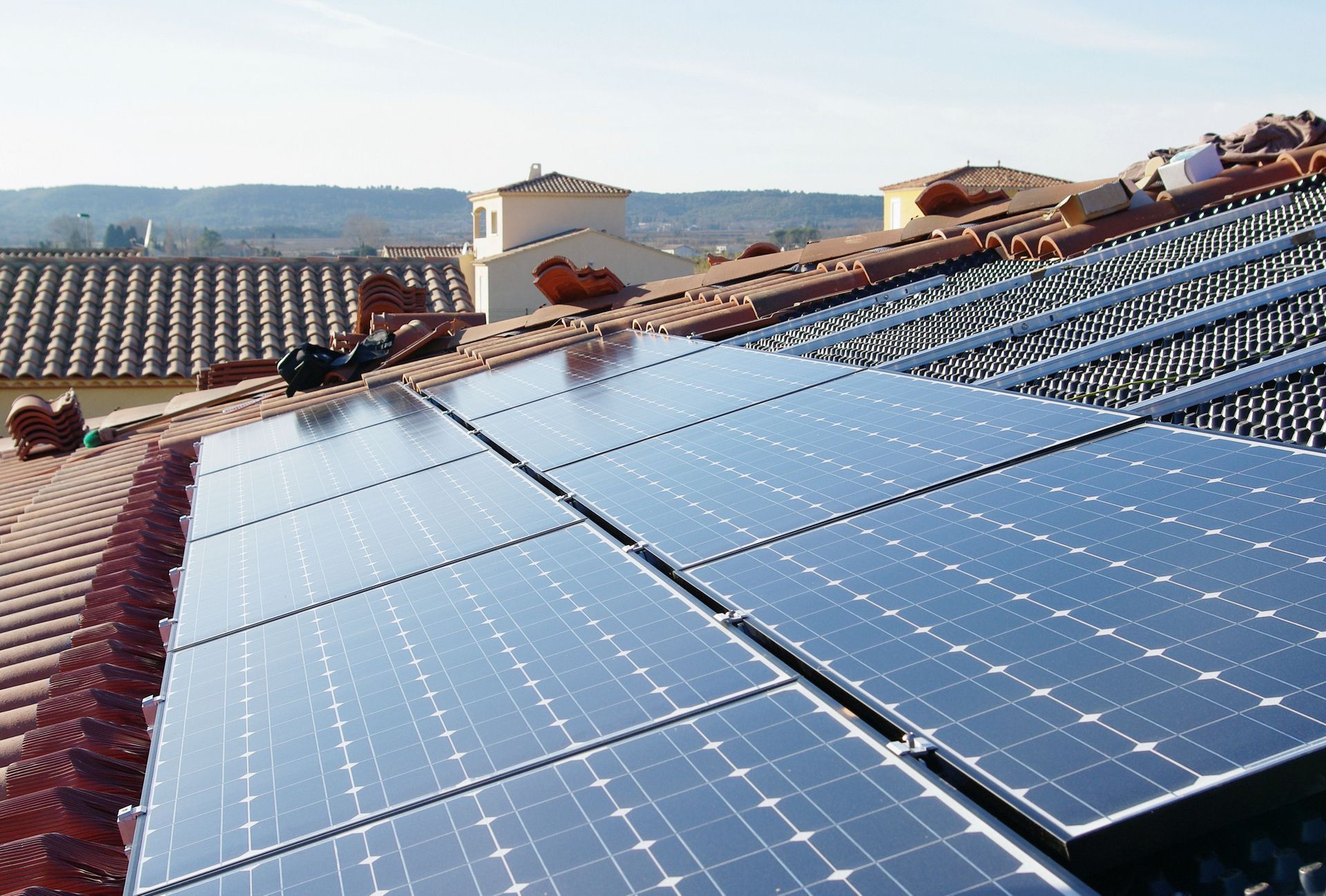 Des panneaux solaires installés sur un toit de tuiles rouges, avec un paysage vallonné au loin en arrière-plan.