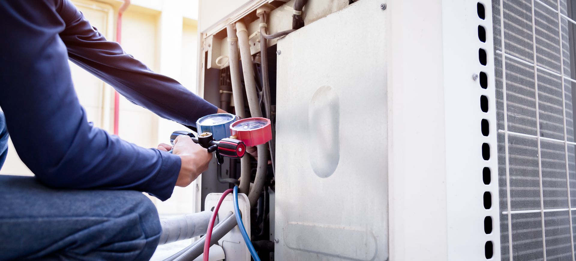 Un technicien utilise des manomètres pour entretenir une unité de climatisation extérieure.
