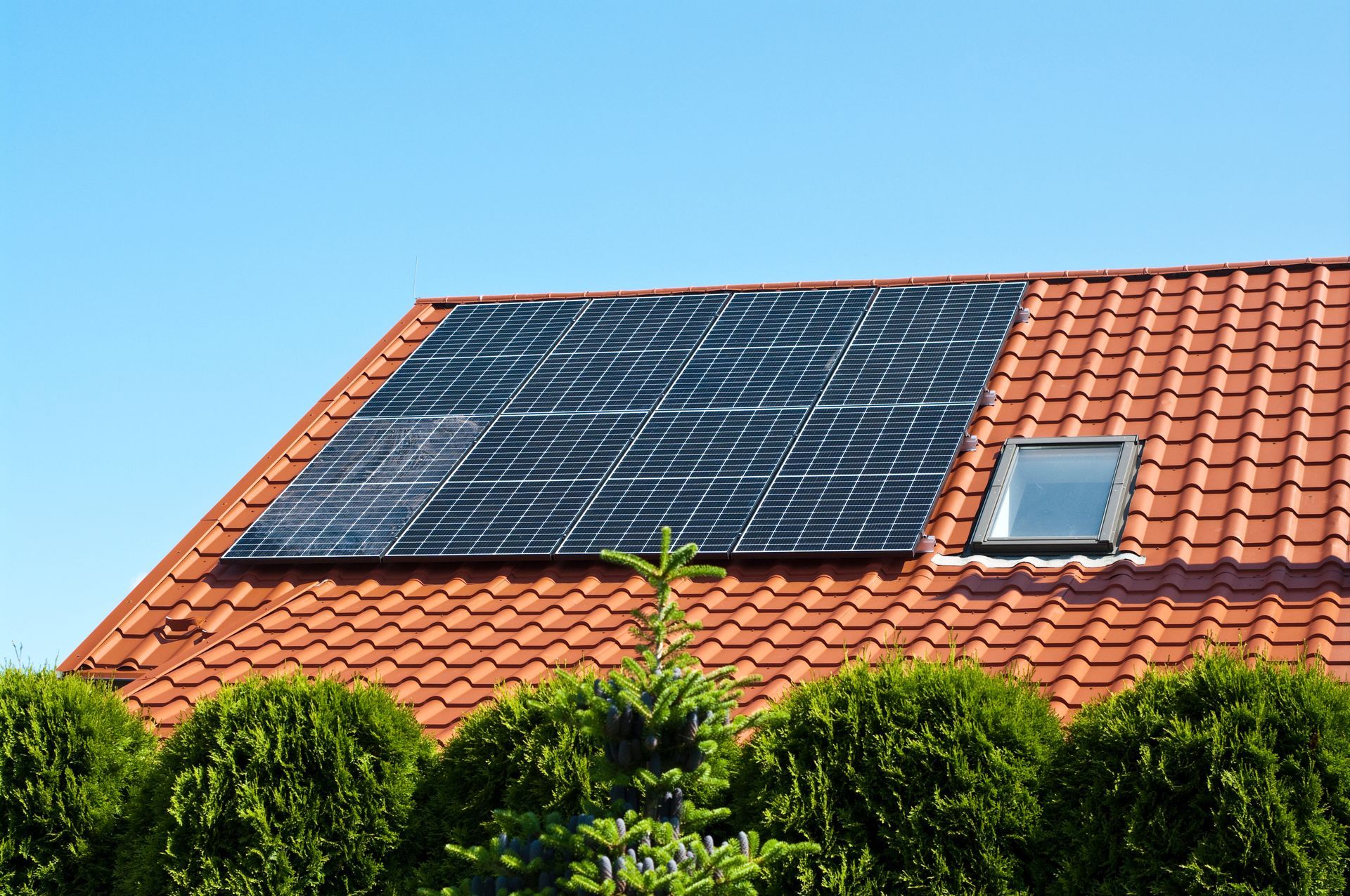 Panneaux solaires sur un toit de tuiles rouges avec un puits de lumière et un ciel bleu.