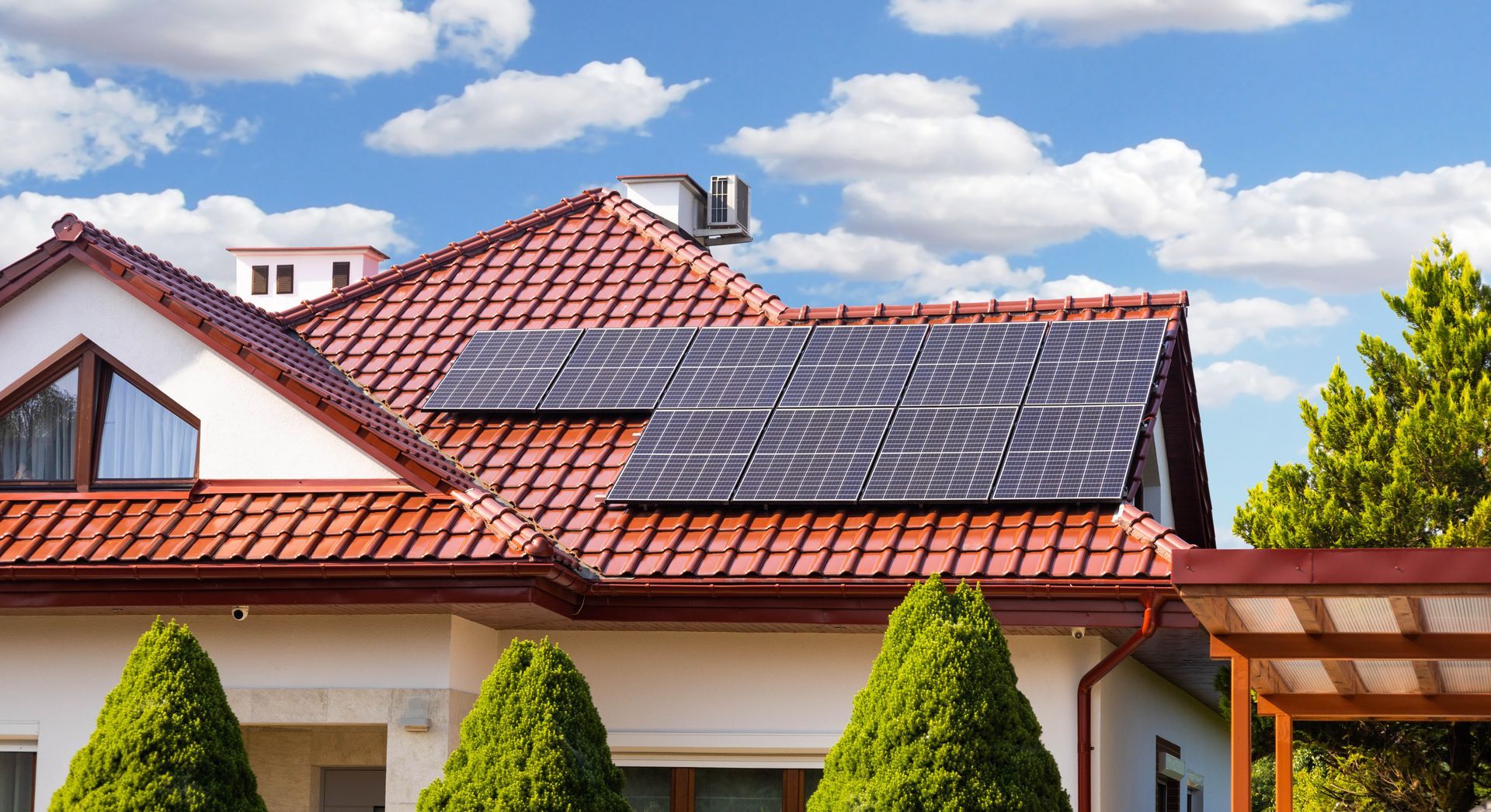 Des panneaux solaires sur le toit de tuiles rouges d'une maison aux boiseries blanches.