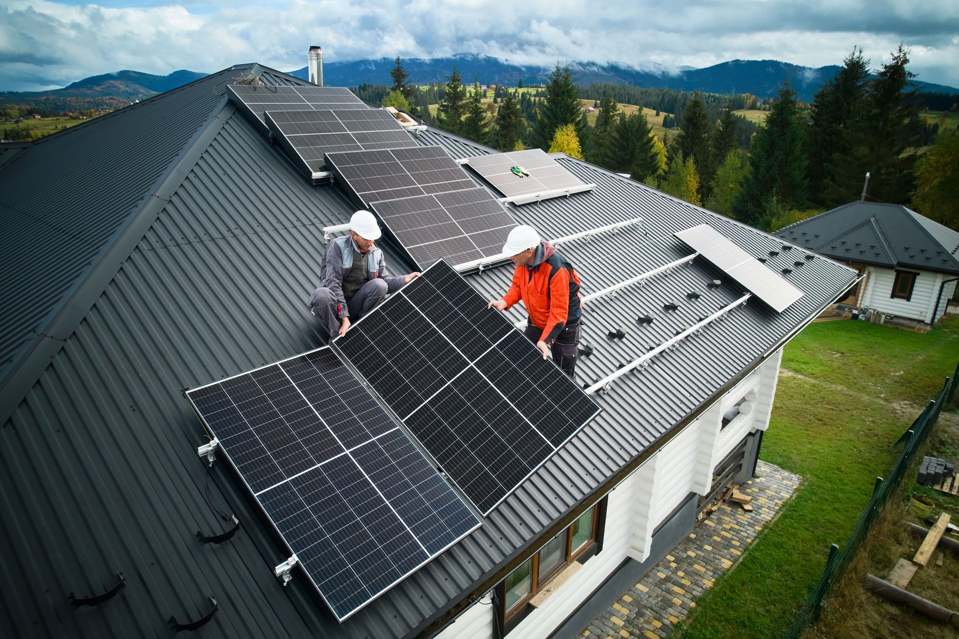 Des ouvriers installent des panneaux solaires sur le toit d'une maison. Montagnes en arrière-plan.