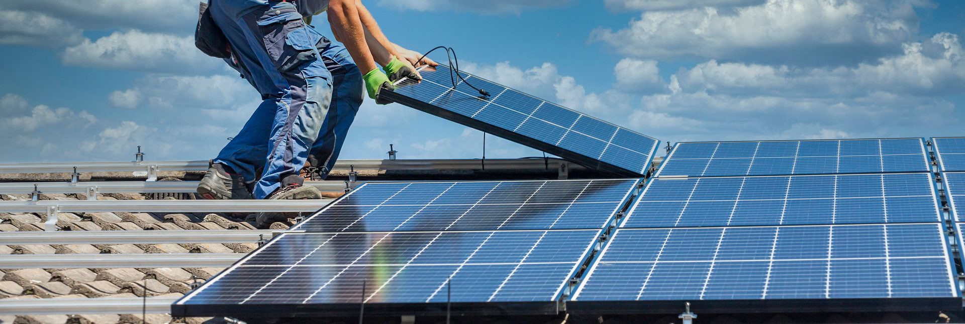 Un ouvrier installe des panneaux solaires sur un toit, ciel bleu en arrière-plan.