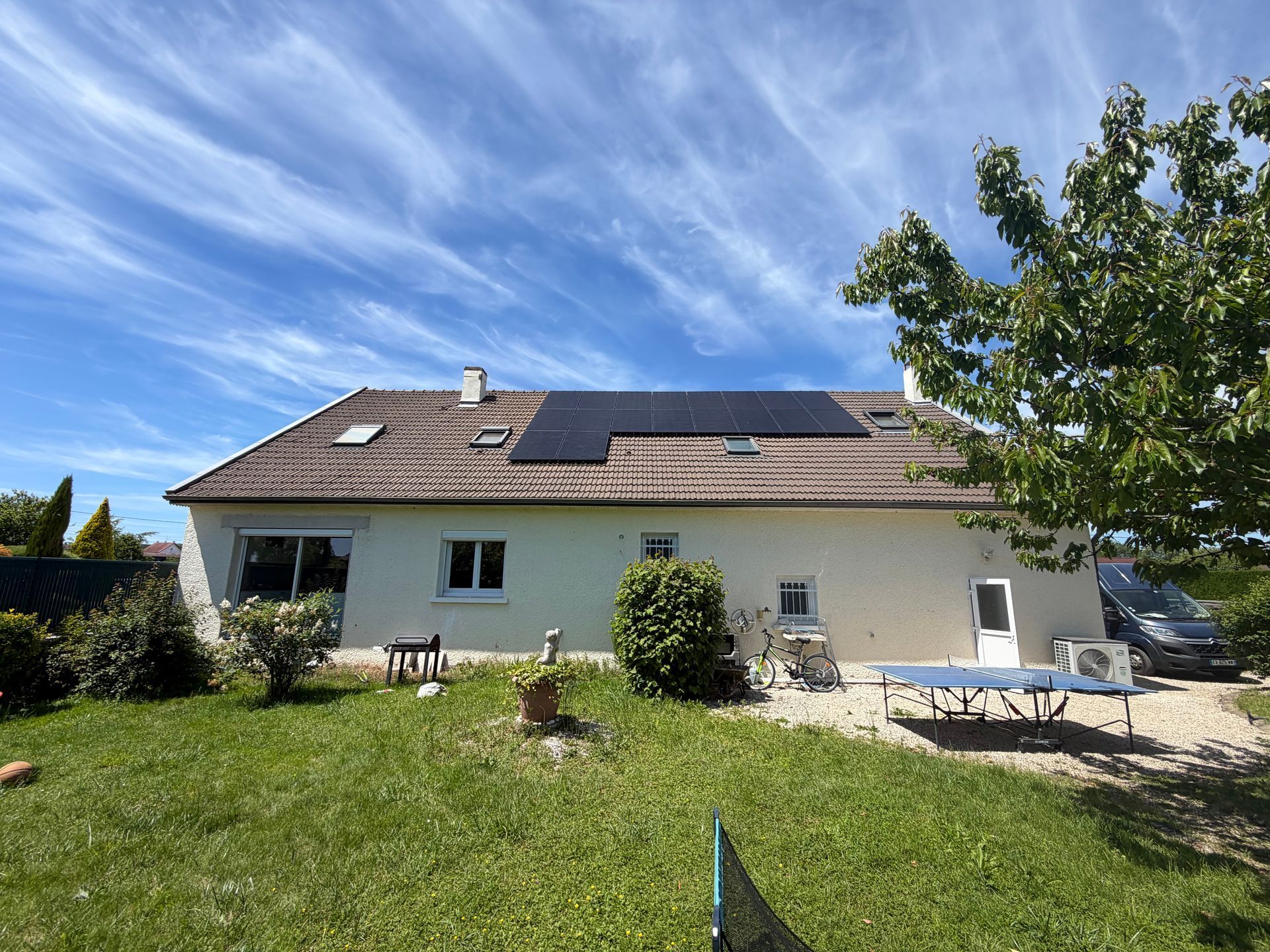 Des panneaux solaires sur le toit de tuiles rouges d'une maison, sous un ciel bleu nuageux.