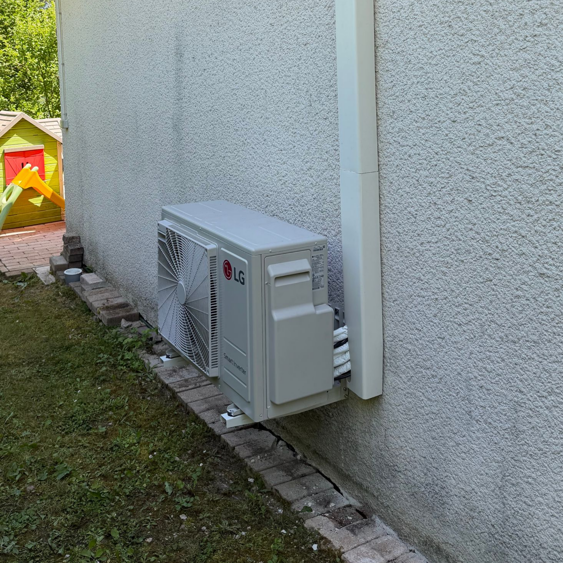 Climatiseur fixé sur un mur blanc au-dessus d'un canapé gris, près d'une fenêtre baignée de lumière naturelle.