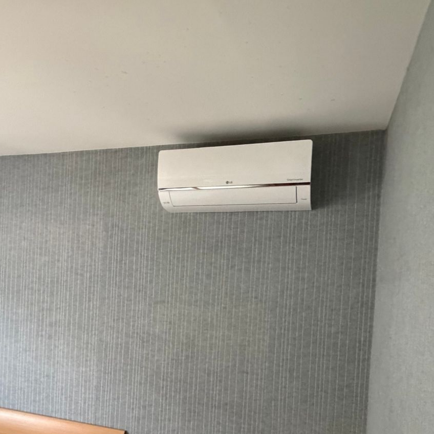 Un climatiseur sur un mur blanc dans un salon moderne, avec un canapé, une lampe et une fenêtre.