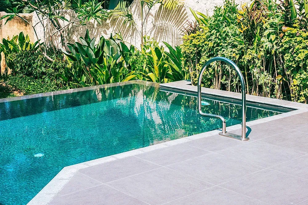 Una gran piscina con una escalera que conduce a ella rodeada de árboles.