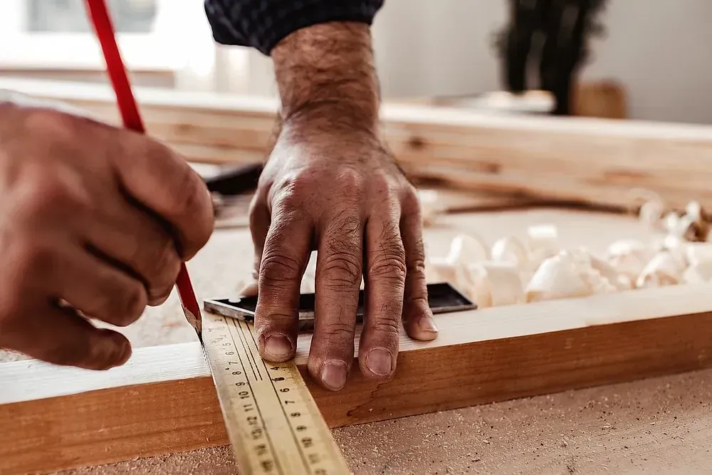 Un hombre está midiendo un trozo de madera con una regla y un lápiz.