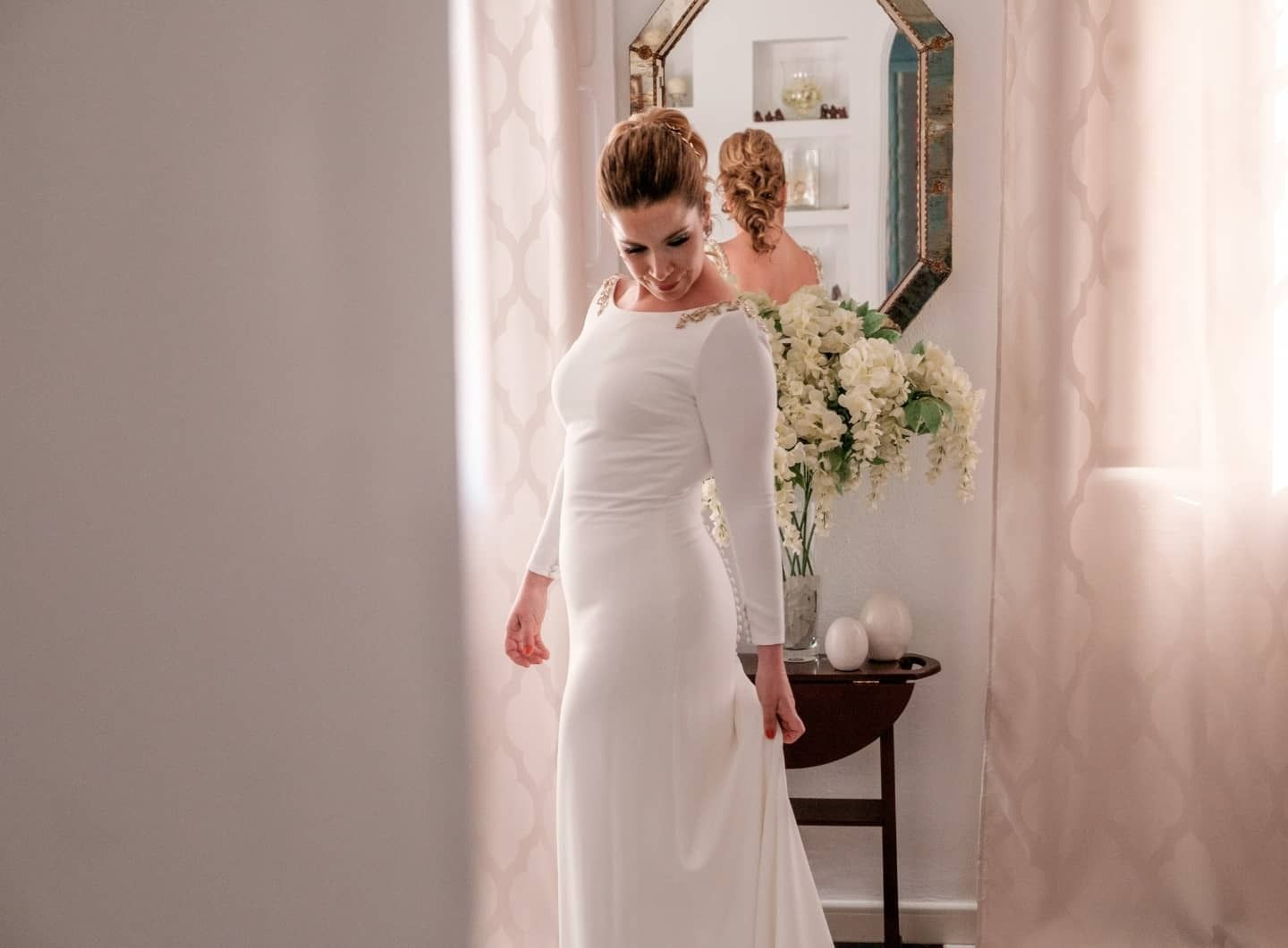 Una mujer con un vestido blanco está parada frente a un espejo.