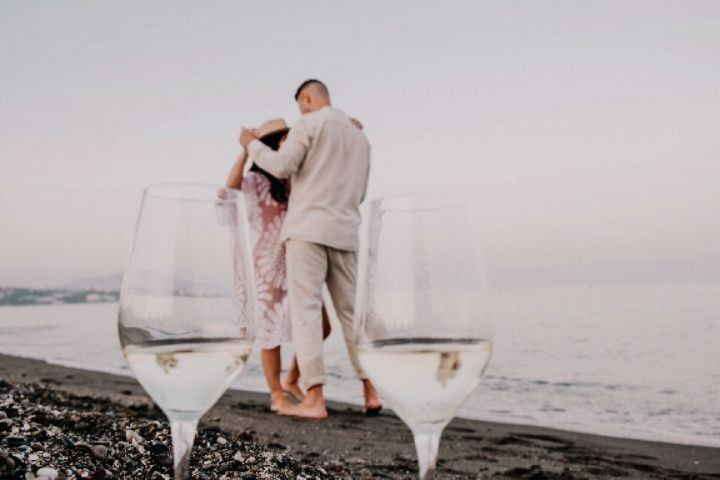 Un hombre y una mujer están de pie en una playa junto a dos copas de vino.