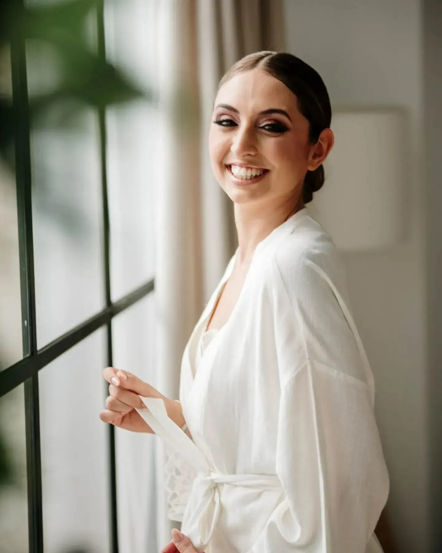 Una mujer con una túnica blanca está parada frente a una ventana.