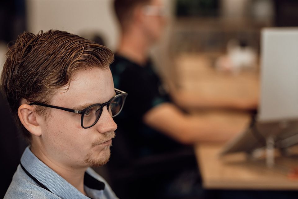 Een man met een bril zit aan een bureau voor een computer.