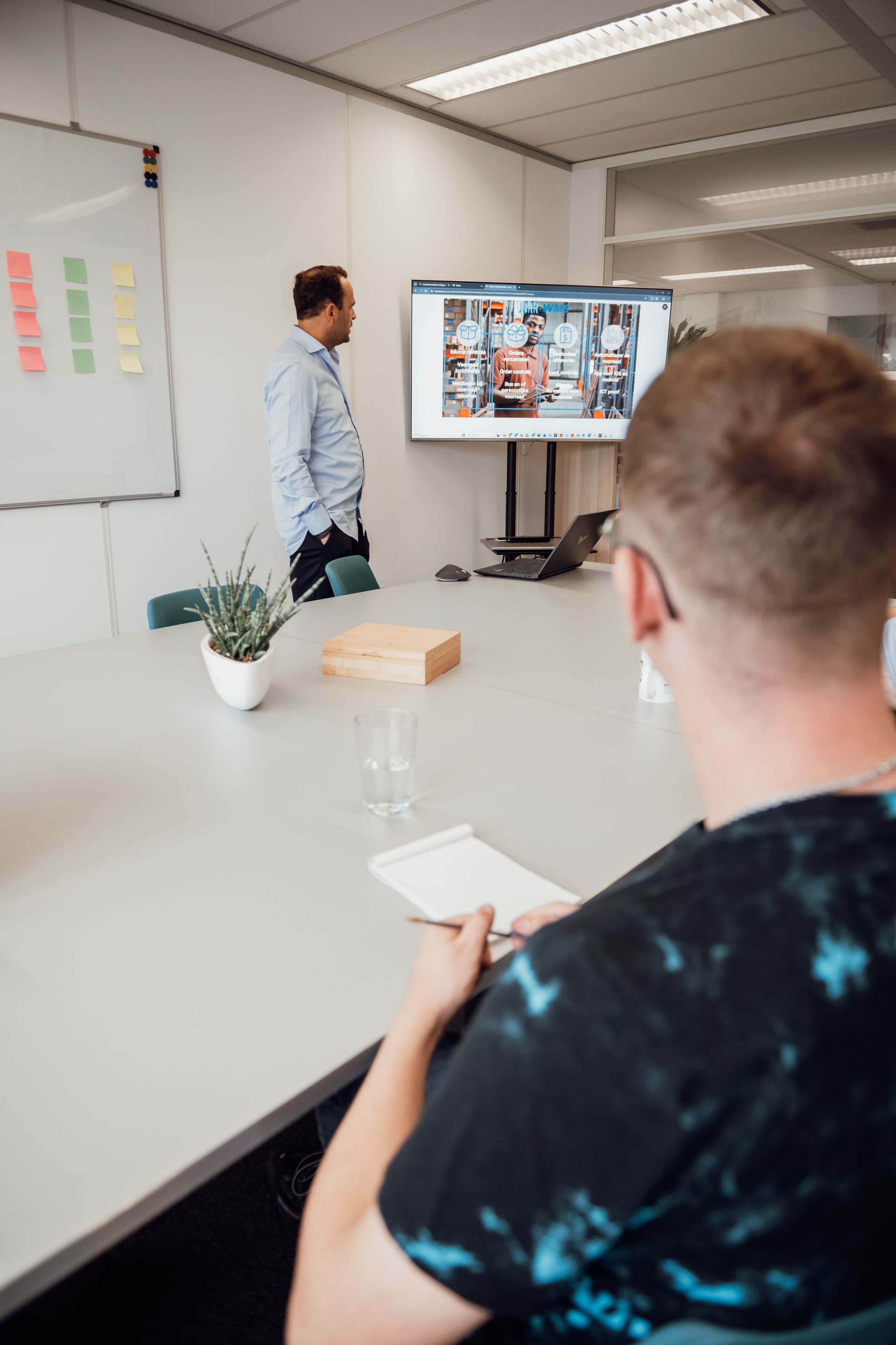 Een man staat voor een groot scherm in een vergaderruimte.