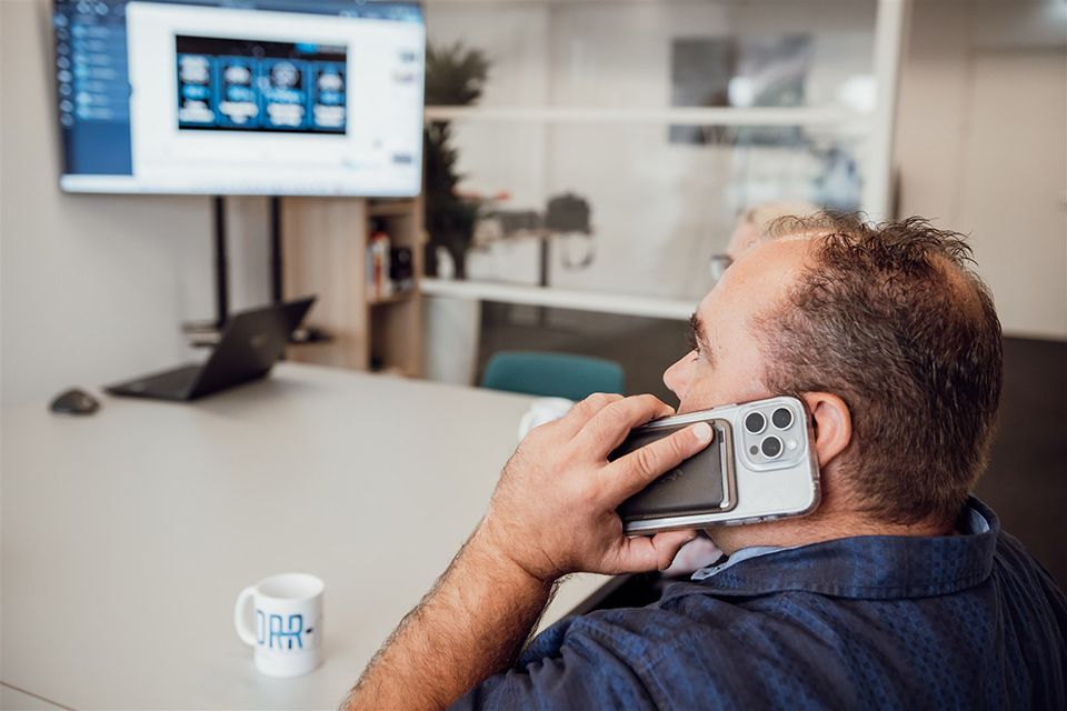 Een man zit aan een tafel en belt via een mobiele telefoon.