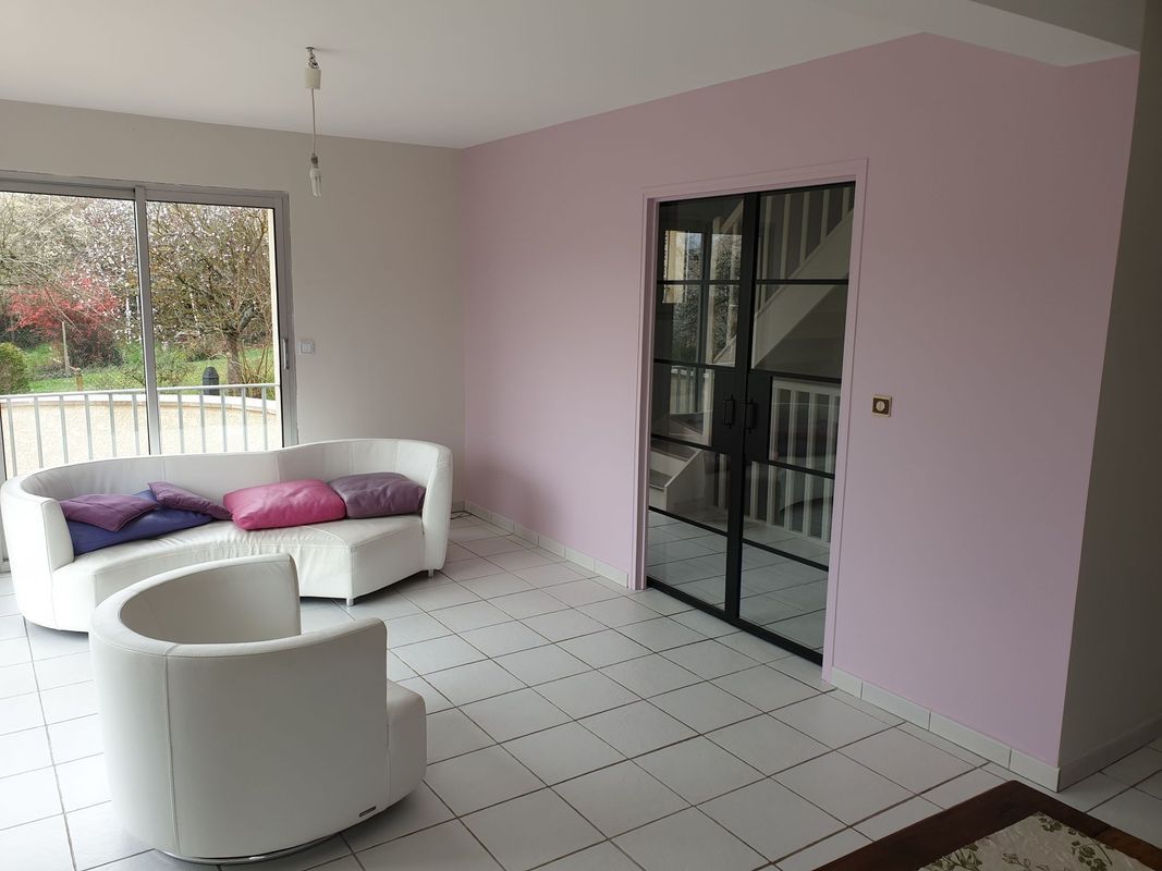 Salon avec meubles blancs, mur rose et portes vitrées noires.