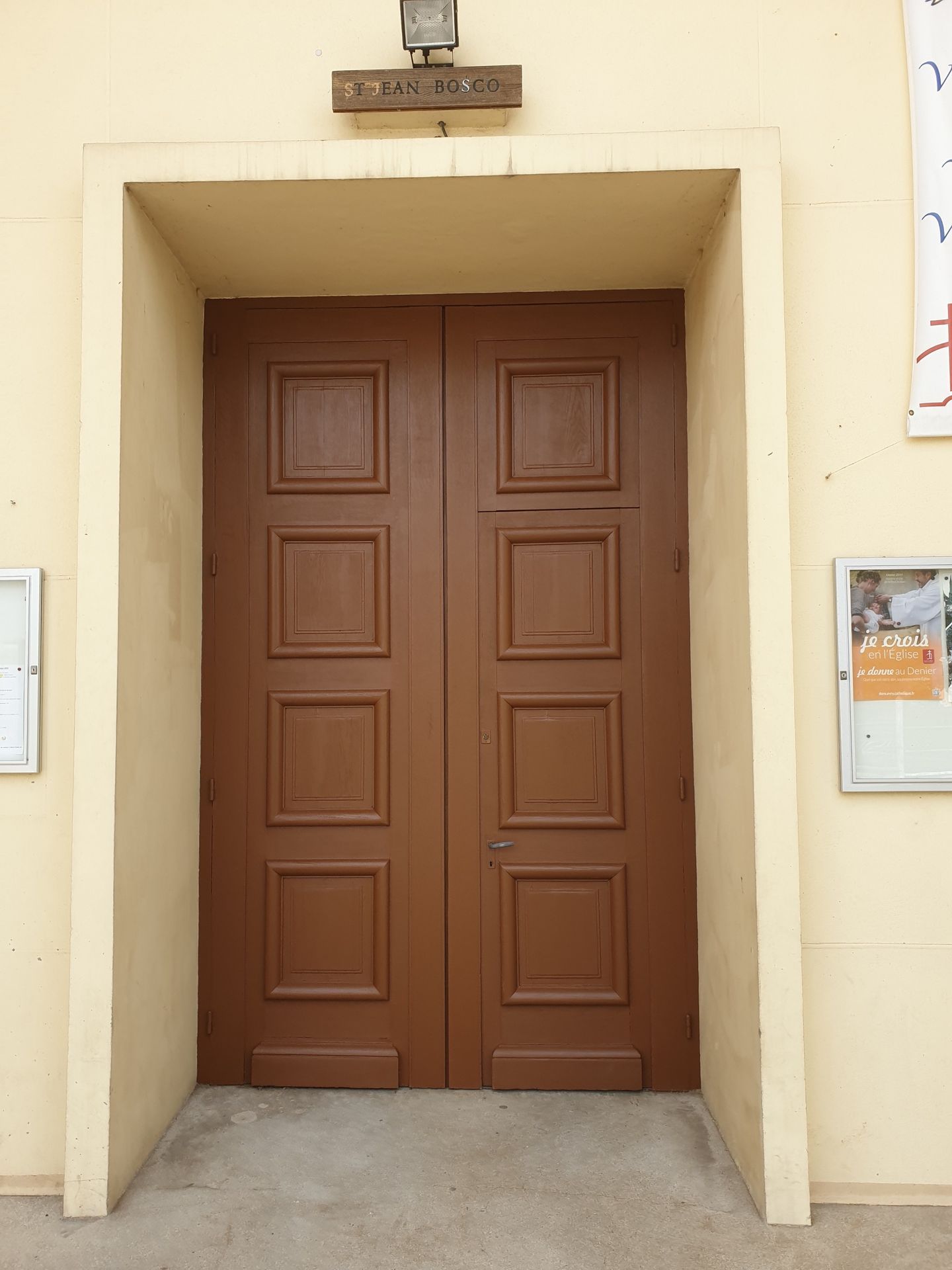 Double porte marron dans un encadrement beige, avec une petite pancarte au-dessus.